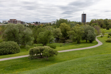 View of urban park with walking paths, pond, and city buildings in Ottawa, Canada in spring