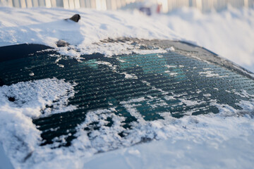 Close up of car rear window with snow and ice melting, defroster lines visible under wet glass with water droplets, winter vehicle detail in sunlight