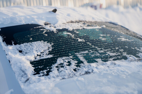 Rear car window with snow buildup and thawing ice, detailed defroster stripes and droplets on glass surface, close up automotive winter conditions scene