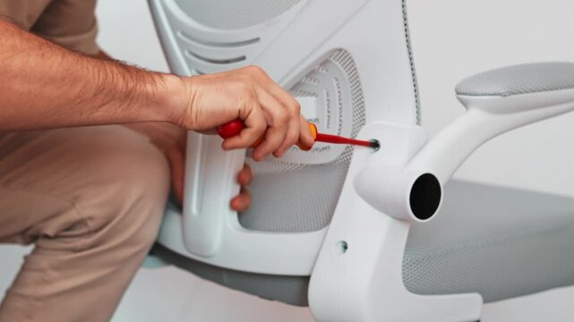 Worker fixes chair part during diy installation, tightening hardware ensure strong structure. Closeup captures careful tool handling and repair accuracy essential for practical home furniture setup.