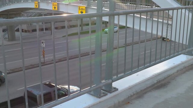 Cars on a multilane highway driving inflow motion through a city on a sunny day with a metal railing in the foreground