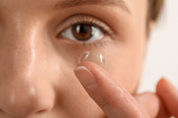 Woman putting on contact lenses against light background, closeup
