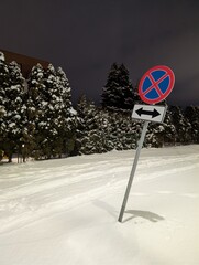 Road sign standing in a snowy landscape at night. Winter traffic scene with cold weather, safety and transportation concept.