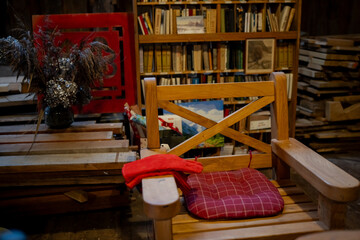 Empty wooden chair with padded red cushion in creative workshop space, stacks of boards, dried flowers and library shelves creating warm handcrafted atmosphere