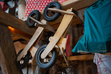 Two wooden toddler balance bikes hanging upside down in shed interior, black tires and simple frames, indoor storage of kids toys in rural outbuilding