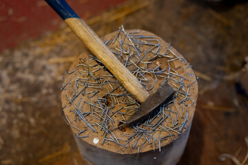 Hammer resting on wooden stump covered with scattered nails and bent wire fasteners, close up carpentry work surface in workshop with shallow depth of field