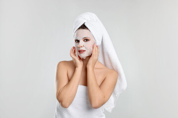 Woman with hair wrapped in towel and facial mask on light grey background