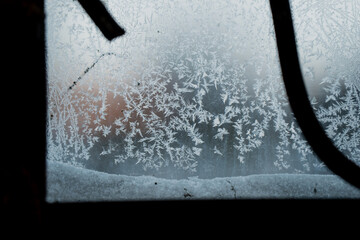Frozen window surface covered in frost crystals, decorative iron bars in foreground and soft bokeh outside, minimalist winter cold texture detail shot