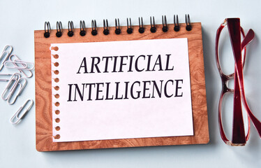 ARTIFICIAL INTELLIGENCE - words on a white sheet of paper on the background of a notebook, glasses and paper clips