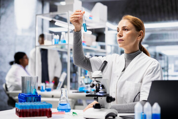 Quality control analyst in lab inspecting blue liquid clarity in test tube against light. Laboratory worker verifying chemical purity standards for industrial product manufacturing process