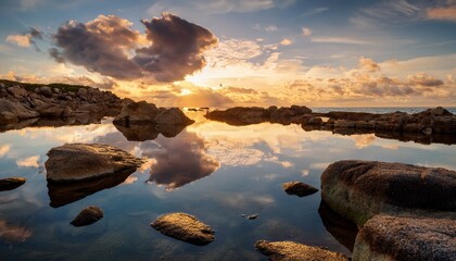 tranquil reflection of clouds and rocks on still water at a serene coastal location during golden hour