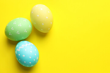 Many painted Easter eggs on yellow background, flat lay. Space for text