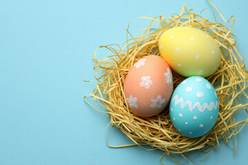 Obraz premium Many painted Easter eggs and straw on light blue background, top view. Space for text