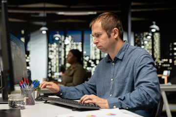 Male engineer arranging virtual assets in architectural software on computer, creating a detailed 3D render of a floor plan. Freelancer uses program for computer aided interior design.