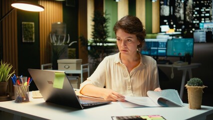 Fototapeta premium Executive assistant scheduling a presentation and planning meetings with calendar, solving tasks for the company at night. Demonstrates executive insight focused on targets. Camera A.