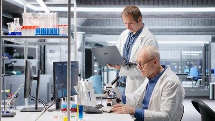 Senior chemist and coworker observing specimen under microscope in the laboratory. Clinical experiment illustrates discovery process in bioscience and molecular research for innovation.