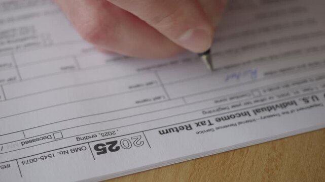 Man Filling In The Tax Form 1040 for 2025 Year. Person Calculates of Planning Budgets Yearly Personal Finance and Fills up US Tax Form 1040 For 2025 Year. Signing 1040 Income Tax Return For 2025 Year.