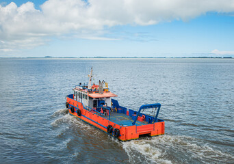 Industrial orange workboat sailing on calm blue sea under a cloudy sky. Rear view of a professional service vessel navigating open coastal waters