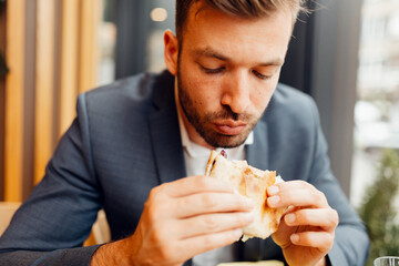 Businessman in a suit eating a delicious sandwich, hungry male professional having a quick lunch break during work.