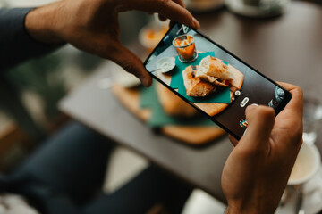 Close-up of a man taking photo of his food with a smartphone, male customer capturing dish for social media in a restaurant.