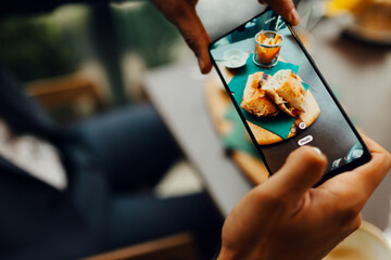 Close-up of a man taking photo of his food with a smartphone, male customer capturing dish for social media in a restaurant.