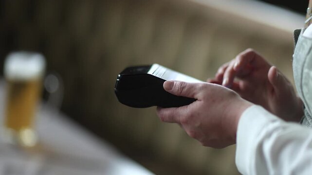 Unrecognizable waitress in a dirndl entering an order on a mobile terminal, modern contactless payment in a tavern