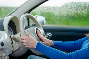 Hands on steering wheel inside a car with rain on the windshield in a countryside area