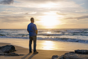 Man stands on beach and watches sunset over the ocean at seaside location in the evening