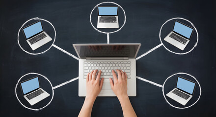Hands typing on laptop connecting to multiple remote computers in hand drawn chalk circles on blackboard for global networking cloud computing and team collaboration concept