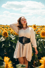 Sunflowers bloom in a field while a woman smiles in front of them on a sunny day during the summer season in a rural area