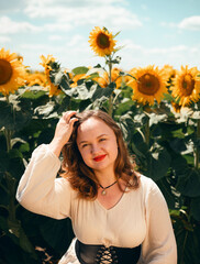 Sunflowers bloom in a field while a woman smiles in front of them on a sunny day during the summer season in a rural area