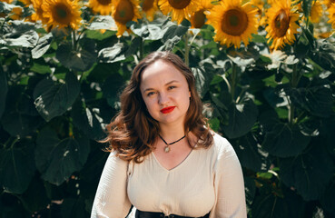 Sunflowers bloom in a field while a woman smiles in front of them on a sunny day during the summer season in a rural area