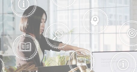 Leaning woman in dark blazer reaching toward laptop at office desk, with digital UI icons
