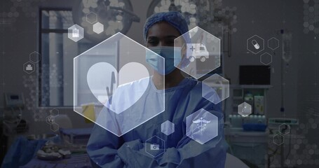 Standing surgeon wearing blue gown, cap, mask crossing arms in OR, showing hexagonal medical UI