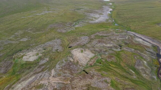 Aerial view of a rocky plateau with small pond, mosaic moss and shallow channel. Wide horizon and low cloud shape a timeless arctic scene. Good for travel, wilderness story, documentary and scienti