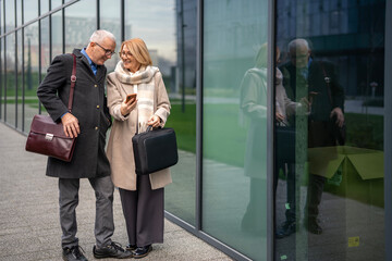 Mature business couple interacting with smartphone outdoors