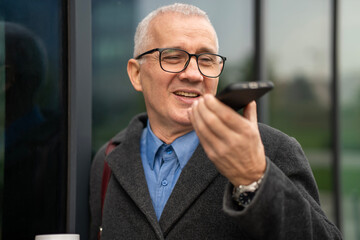 Smiling senior man using smartphone sending voice message