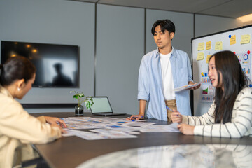 Asian business team meeting in office, male leader presenting data charts to female colleagues, Group brainstorming marketing strategy and financial report, corporate teamwork and planning concept