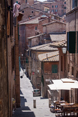 Naklejka premium Historic alleyway in Siena featuring traditional brick houses, shuttered windows, and classic Tuscan urban character. Captured in soft daylight with strong architectural depth.
