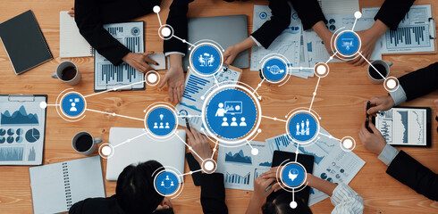 A high-angle view of a collaborative business meeting, showcasing diverse professionals engaged in data analysis, discussions, and strategic planning in a modern office setting. Amity