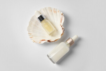 Bottles of cosmetic serum with seashell on white background