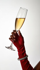 Fototapeta premium Dark skinned hand in red satin glove holds champagne flute. Sparkling wine bubbly drink. Woman wears diamond bracelet, celebrates special event or party.