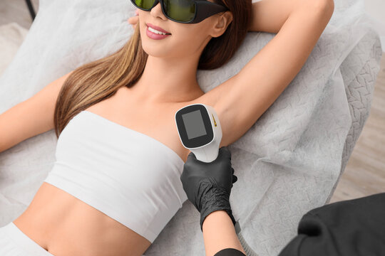Female cosmetologist performing photoepilation on client's underarm in beauty salon