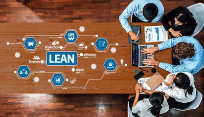 A diverse team collaborates around a table, utilizing technology and data charts to discuss lean production strategies and enhance operational efficiency in business. Amity