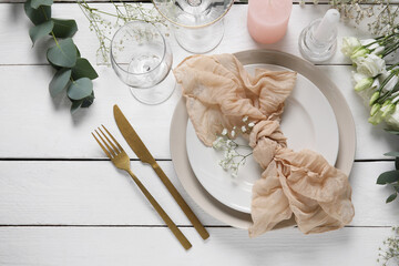 Wedding table setting with napkin, flowers, eucalyptus branches and glasses on white wooden...