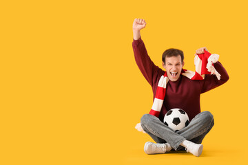 Male soccer fan with scarf and ball sitting on yellow background