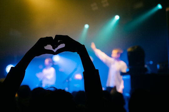 Silhouette hands making heart shape at live concert with blue stage lights