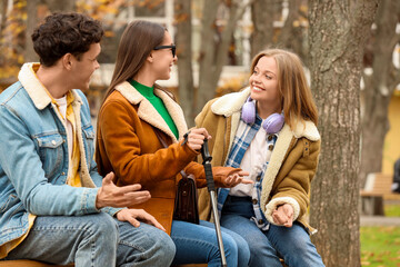 Blind young woman with her friends talking on bench outdoors