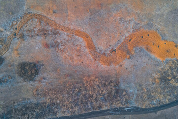 Meandering frozen creek with dry reeds near forest and dirt road in winter landscape aerial drone shot for environmental concept and travel