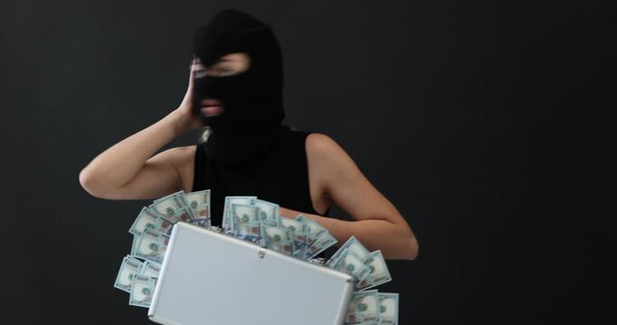 Masked thief with briefcase full of money on black background